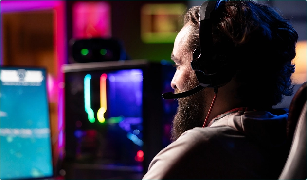 Um homem está sentado atrás do computador, de costas para nós, jogando um jogo.