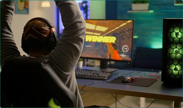 Um homem está sentado atrás do computador, de costas para nós, jogando um jogo.